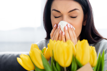 selective focus of woman with pollen allergy sneezing near tulips