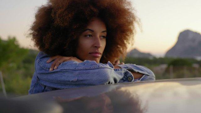 Young woman during road trip leaning on car roof
