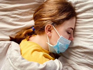a teenage girl in a medical mask in bed during corona virus quarantine time lack of freedom