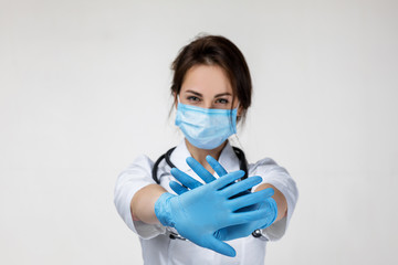 Young woman doctor in mask and rubber gloves doing stop sign on gray background. defense gesture....