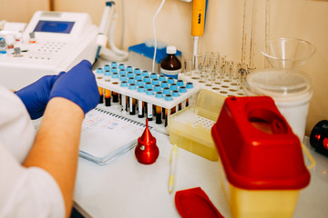 Blood test process in laboratory. Doctor hands making blood test. Many blood test-tubes with blood on the table. Covid-19 testing.