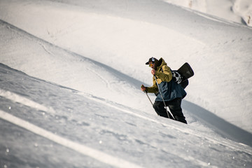 man in glasses with ski equipment and sticks climbs snowy mountain