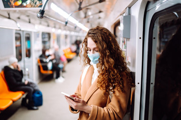 Fototapeta na wymiar Girl in protective sterile medical mask on her face with a phone in a subway car. Woman using the phone to search for news about coronavirus. The concept of preventing the spread of the epidemic.