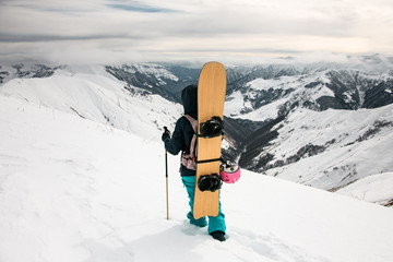 Staying snowboarder on the background of snow-capped mountains and cloudy sky.