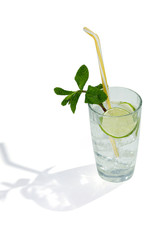 Mojito cocktail with ice cubes is contained in a highball glass with a straw, lime slices and a sprig of mint. The showy illustrative picture is made on the white background.