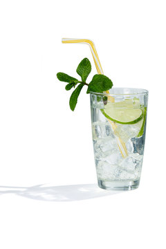 Mojito cocktail with ice cubes is contained in a highball glass with a straw, lime slices and a sprig of mint. The showy illustrative picture is made on the white background.