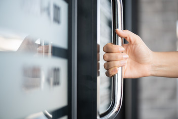 Closeup woman hand holding the door bar to open the door with glass reflection background. - obrazy, fototapety, plakaty