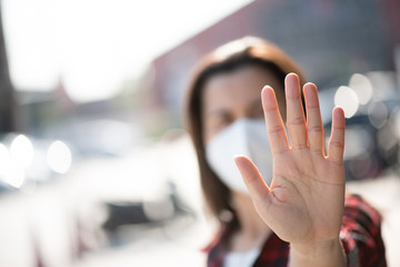 Close up of woman wearing protective face mask, get ready for Coronavirus and pm 2.5 fighting and show stop hands gesture for stop corona virus outdoor beside road in background.