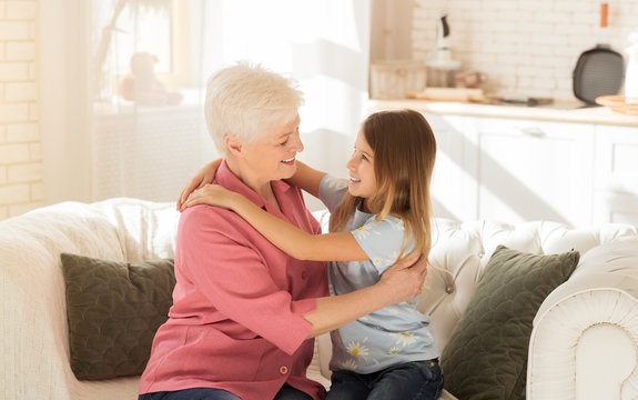 Little Child And Her Grandmother Hugging Each Other On Sofa