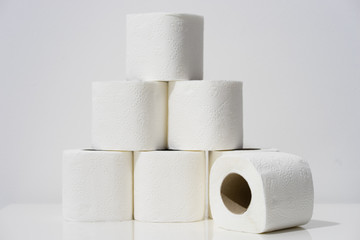 Front view on white toilet paper rolls stacked on the table in front of the wall background