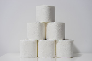 Front view on white toilet paper rolls stacked on the table in front of the wall background