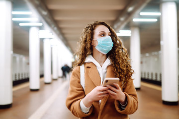 Girl in protective sterile medical mask with a phone  at subway station. Woman, wear face mask,...