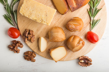 Smoked cheese and various types of cheese with rosemary and tomatoes on wooden board on a white background . Top view.