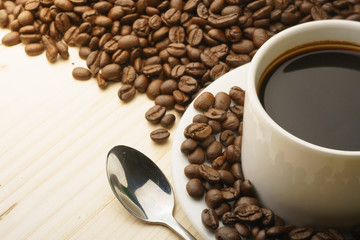 close up on coffee cup with coffee beans and steel spoon on wooden table. free copy space for your...