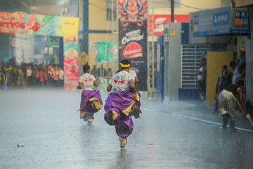 young boys in flamboyant carnival costumes run under strong rain by city street