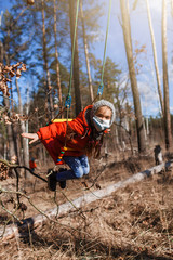 A cute 6-7 years old girl in red coat wearing respirator mask flying on the swing alone in the forest