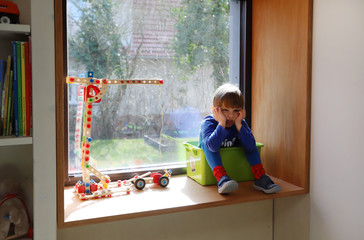 Ein vierjähriger Junge sitzt gelangweilt in seinem Zimmer am 18.03.2020. - obrazy, fototapety, plakaty