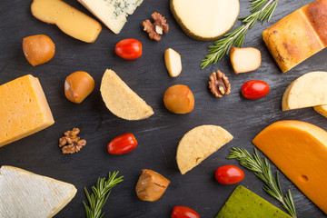 Set of different types of cheese with rosemary and tomatoes on a black wooden background . Top view.