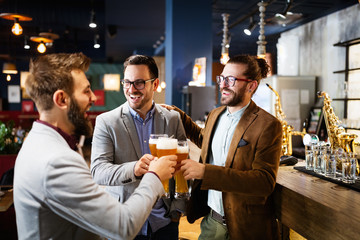 Young businessmen are drinking beer, talking and smiling while resting at the pub