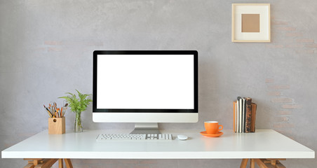 Workspace computer monitor with white blank screen putting on white working desk with books, coffee cup, potted plant, pencil holder, wireless keyboard and mouse. Orderly workplace concept.