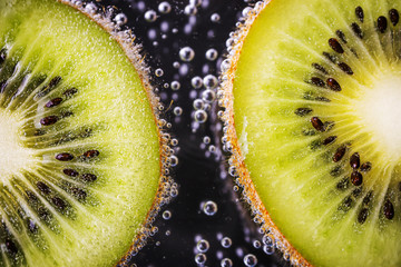 A slices of ripe juicy kiwi in mineral water. Detailed macro photo. The concept of summer refreshing drinks, fruits, vitamins. Dark background.
