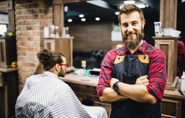 Portrait of happy young barber with client at barbershop and smiling.
