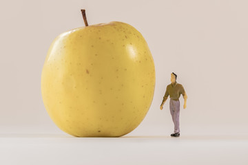 Miniature man figure standing next to big yellow apple. Shallow depth of field background. Healthcare, healthy lifestyles and slimming concept.