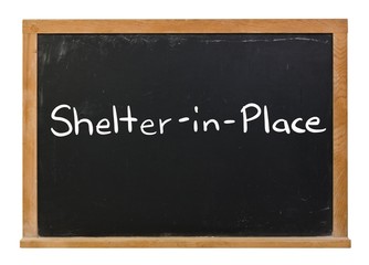 Fototapeta premium Shelter in Place written in white chalk on a black chalkboard isolated on white