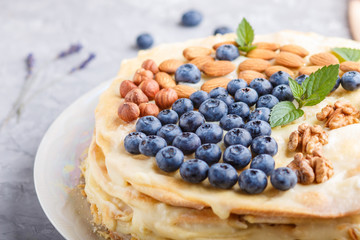 Homemade layered Napoleon cake with milk cream. Decorated with blueberry, almonds, walnuts, hazelnuts, mint on a gray concrete  background. side view.