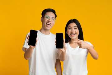 Smiling asian couple showing their smartphones with blank screens