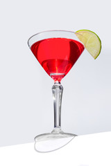 Cosmopolitan cocktail is contained in a martini glass with a lime slice on the rim and isolated on the table edge. The showy illustrative picture is made on the gray background.