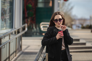 cheerful woman on a city street drinks coffee on a sunny day and looks at the camera. coffee to go. Portrait of a girl with a drink in hands