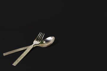 Made of stainless steel, spoon and fork together arranged or isolated on a black background