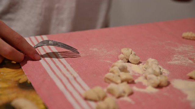 Homemade preparation of potato dumplings. The hands of a Caucasian boy take a piece of pasta and pass it on the back of a fork to give it the characteristic shape.