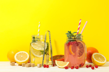 Glass jars with lemonade and ingredients against yellow background. Fresh drink