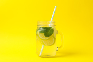Glass jar with lemonade on yellow background. Fresh drink