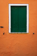 Window with closed green shutters on an orange wall
