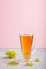 Glass of green grape juice on a gray and pink background. Side view, copy space.