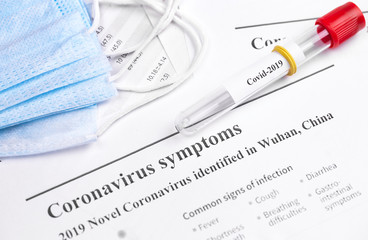 Coronavirus (Covid-2019) on the glass tube with respirator masks on work papers background closeup