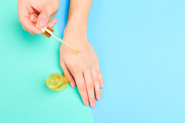  Beautiful young woman's hands with  oil bottle  on pastel background .