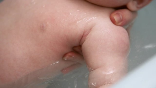 Newborn baby bath. Mother holding a baby to float in warm water. Selective soft focus, slow motion