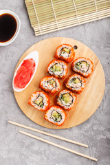 Japanese maki sushi rolls with flying fish roe on wooden board on a gray concrete background. Top view, close up.