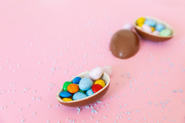 Broken Easter chocolate eggs and colorful decorations on a light background. Banner. Easter concept, easter treats. Flat lay, top view