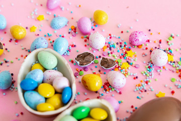 Fototapeta na wymiar Broken Easter chocolate eggs and colorful decorations on a light background. Banner. Easter concept, easter treats. Flat lay, top view
