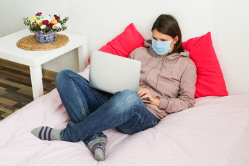 Young woman working at home during quarantine. Sick woman wearing face mask with laptop at home.