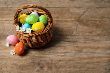 Colorful Easter eggs in basket and flowers on wooden background. Space for text