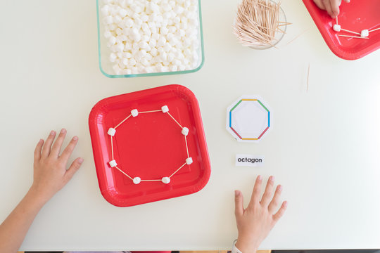 Directly above view of young children making geometric shapes with marshmallows and toothpicks as part of homeschool STEM lesson
