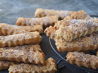 Home cooking. Shortbread Sticks sprinkled with sugar and poppy seeds on a metal grate on a dark background. Close-up.