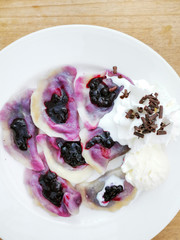delicious sweet polish dumplings stuffed with blueberries jam and blueberries for toppings served with vanilla ice cream and Whipped cream in white plate