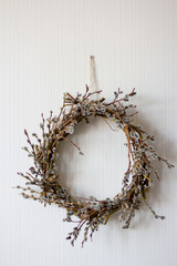 a wreath of willow twigs with fluffy buds made with your own hands hangs on a white wall, vertical frame © Elena